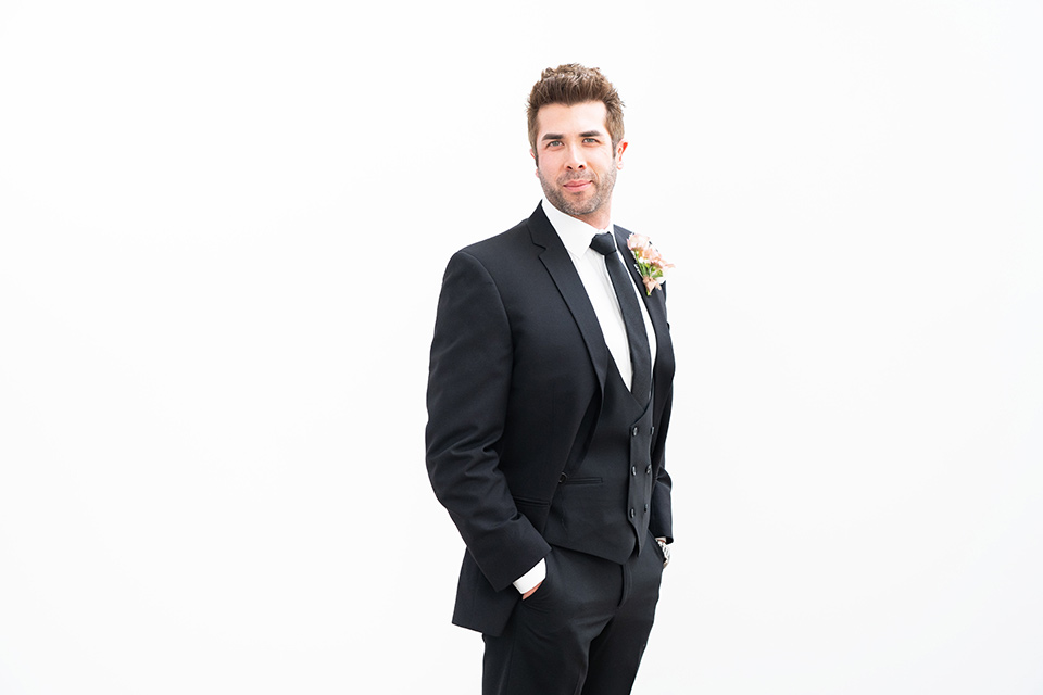  the groom in a black suit with a long black tie 