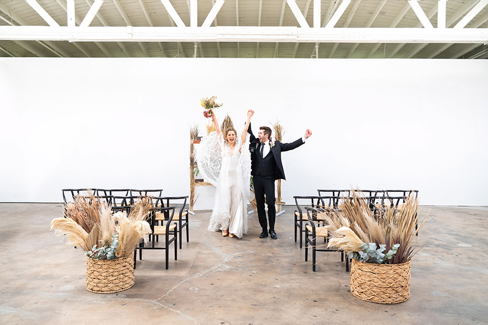  the bride in a lace white gown with long sleeves and a flowing skirt with hair in a modern low bun and the groom in a black suit with a long black tie 