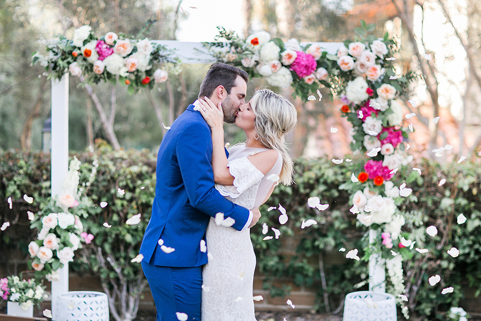  groom in a cobalt blue suit with a black long tie and brown shoes and the bride in a white bohemian gown with a high neckline and cold shoulder detail at the ceremony
