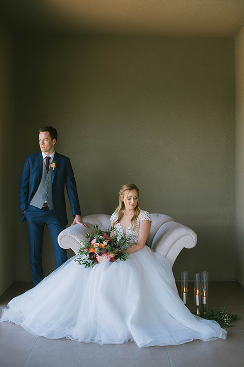  the bride in a flowing a line gown with a lace bodice in a low cut neckline and the groom in a dark blue suit with a grey vest and burgundy long tie