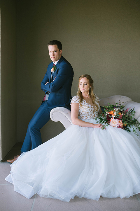  the bride in a flowing a line gown with a lace bodice in a low cut neckline and the groom in a dark blue suit with a grey vest and burgundy long tie 