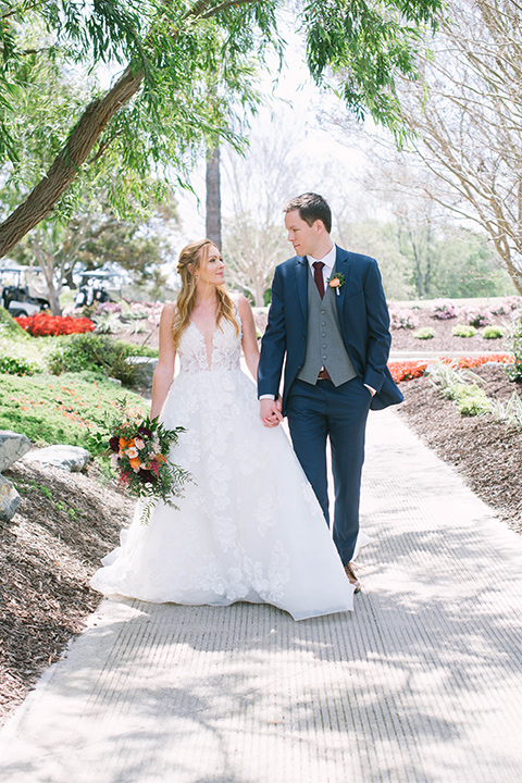  the bride in a flowing a line gown with a lace bodice in a low cut neckline and the groom in a dark blue suit with a grey vest and burgundy long tie 