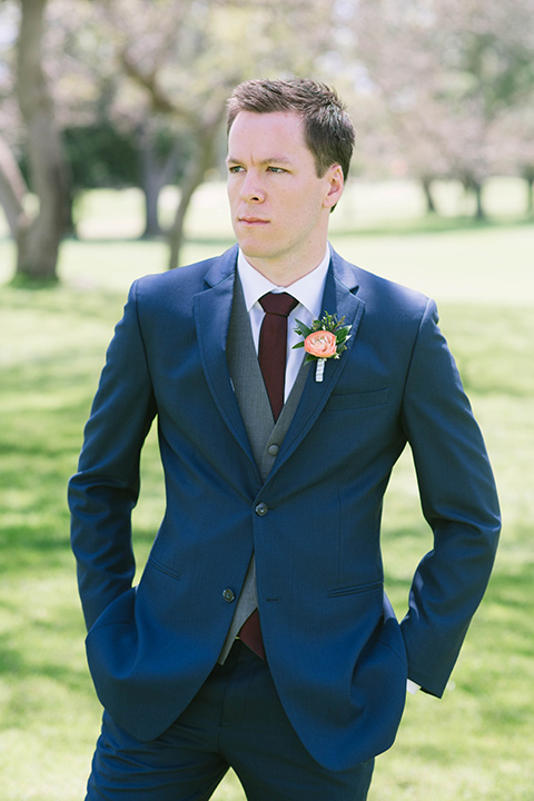  the groom in a dark blue suit with a grey vest and burgundy long tie