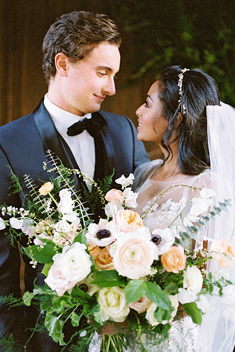  couple close groom in a navy blue tuxedo with a black bow tie and the bride in a white lace flowing gown and a long cathedral veil 