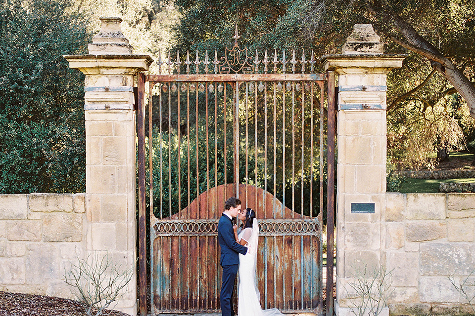  couple close groom in a navy blue tuxedo with a black bow tie and the bride in a white lace flowing gown and a long cathedral veil 