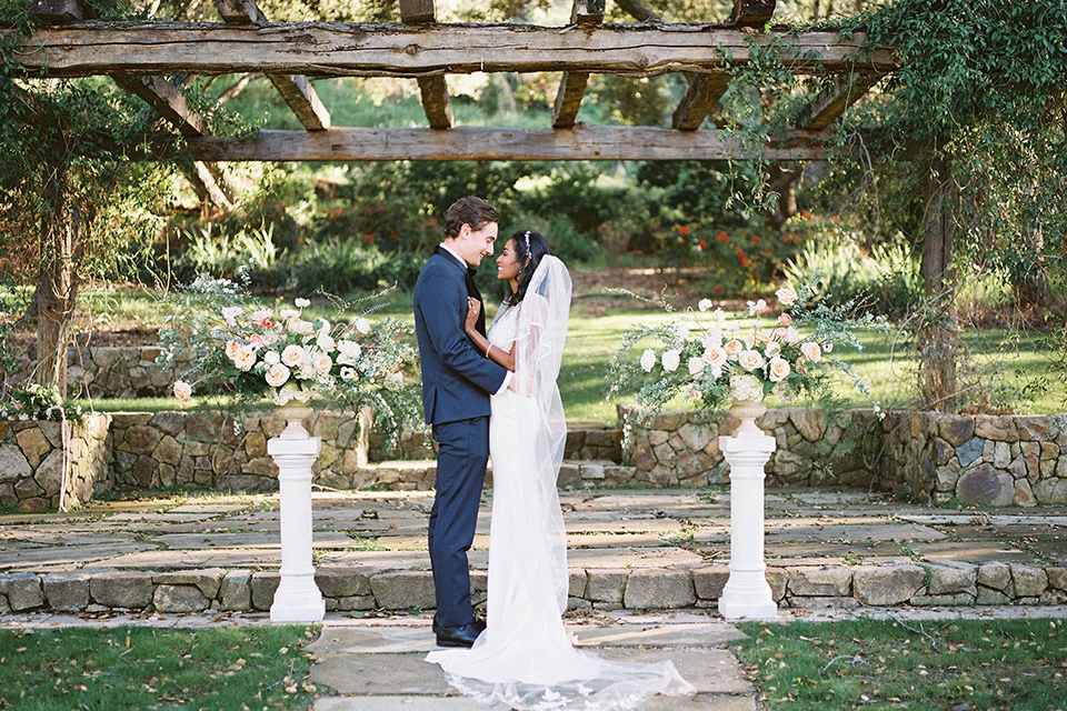  couple close groom in a navy blue tuxedo with a black bow tie and the bride in a white lace flowing gown and a long cathedral veil 