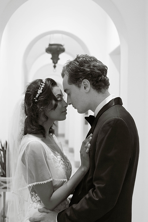  couple close groom in a navy blue tuxedo with a black bow tie and the bride in a white lace flowing gown and a long cathedral veil 