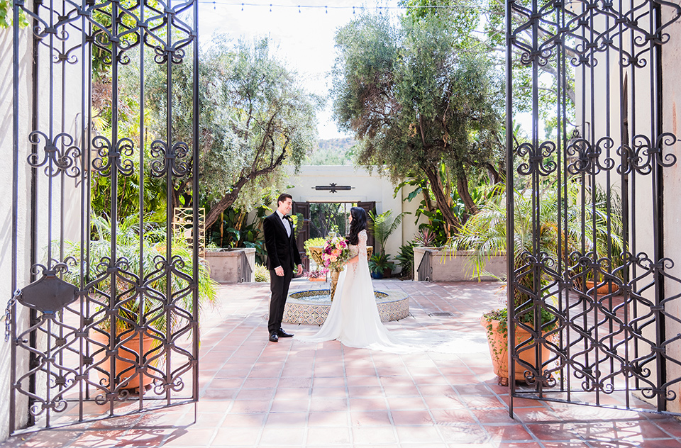  bride in a long gown with a flowing train and cape groom in a black velvet tuxedo with a black bow tie 