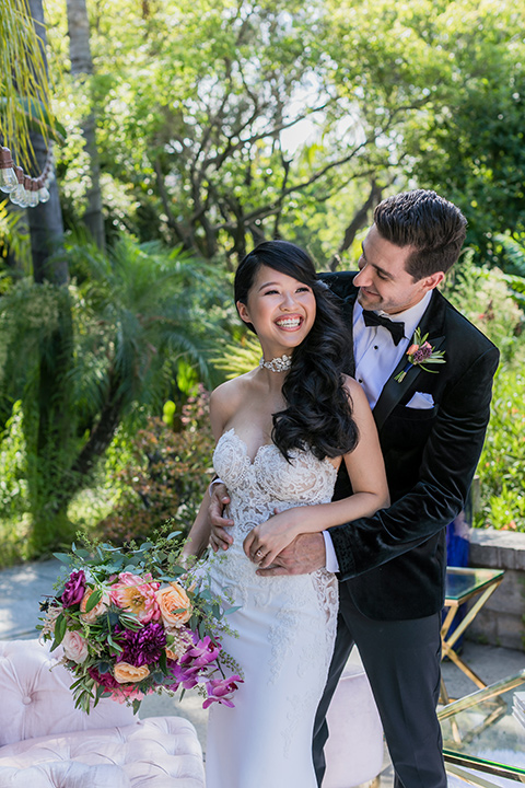  bride in a long gown with a flowing train and cape groom in a black velvet tuxedo with a black bow tie 