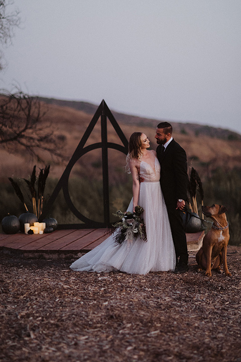  bride in a tulle a line gown with a sweetheart neckline and a crystal bodice and the groom in a black velvet tuxedo and black bow tie by ceremony altar 