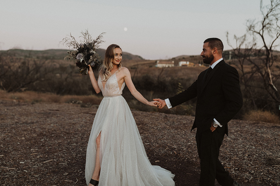  bride in a tulle a line gown with a sweetheart neckline and a crystal bodice and the groom in a black velvet tuxedo and black bow tie sitting at table