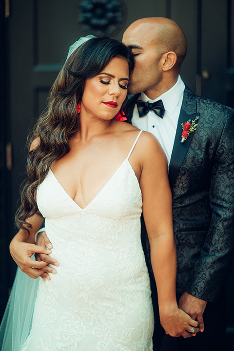  bride in a formfitting gown with a bright red lip and the groom in a black paisley tuxedo with a black bow tie