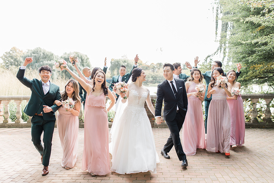  bride in a tulle ballgown with a plunging neckline and a loose bun, bridesmaids in light pink gowns, groomsmen in dark green suits and groom in a black suit with a black long tie