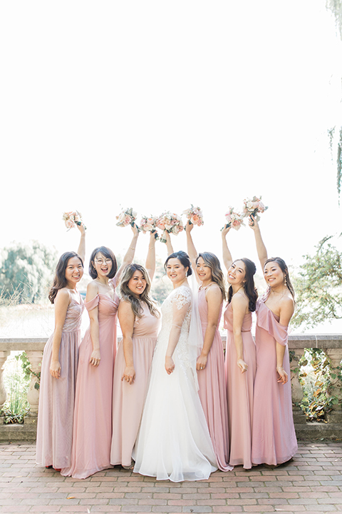  bride in a tulle ballgown with a plunging neckline and a loose bun and bridesmaids in pink gowns 