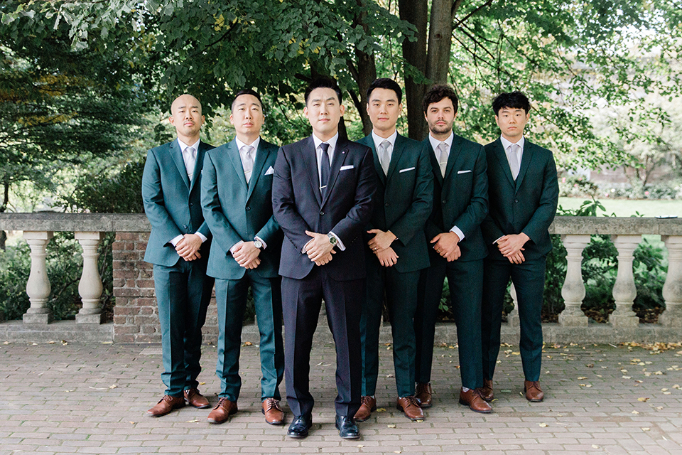  groomsmen in dark green suits and groom in a black suit with a black long tie