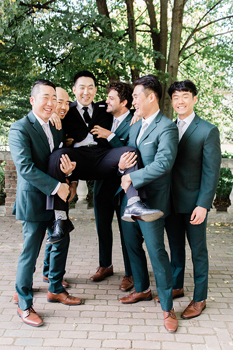  groom in a black suit and long tie, groomsmen in dark green suits