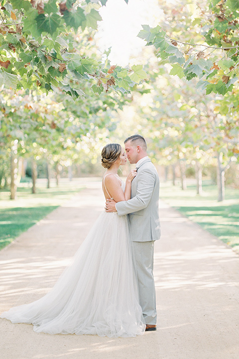  bride in a blush tulle ballgown with thin straps and hair up in a loose bun and the groom in a light grey suit with a white tie