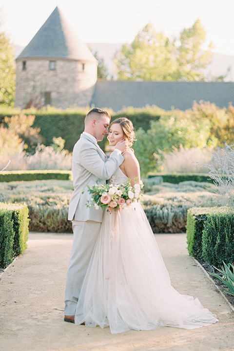 bride in a blush ballgown with thin straps and the groom in a grey suit with a white long tie embracing