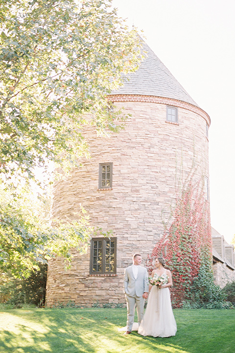 bride in a blush ballgown with thin straps and the groom in a grey suit with a white long tie walking past building