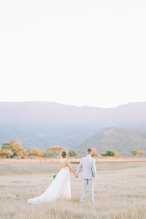 bride in a blush ballgown with thin straps and the groom in a grey suit with a white long tie walking away