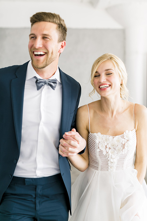  bride in a flowing modern tulle gown and the groom in a slate blue suit with grey velvet bow tie 