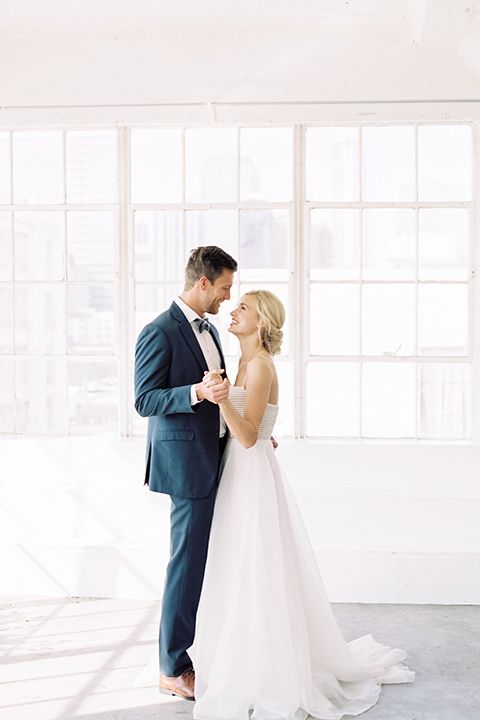  bride in a flowing modern tulle gown and the groom in a slate blue suit with grey velvet bow tie 