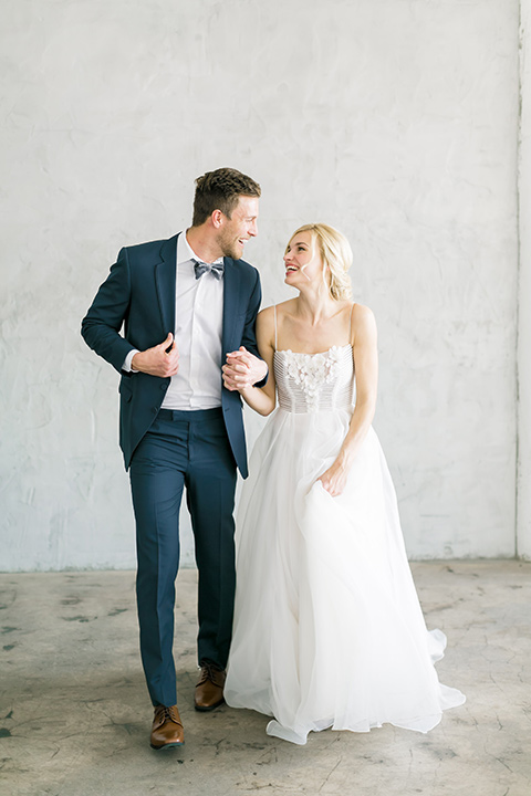  bride in a flowing modern tulle gown and the groom in a slate blue suit with grey velvet bow tie 