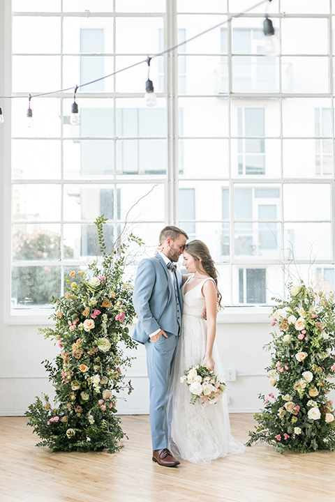 bride and groom at the ceremony, the bride in a flowing white gown with a lace detailing and straps.  The groom in a light blue suit with a grey velvet bow tie