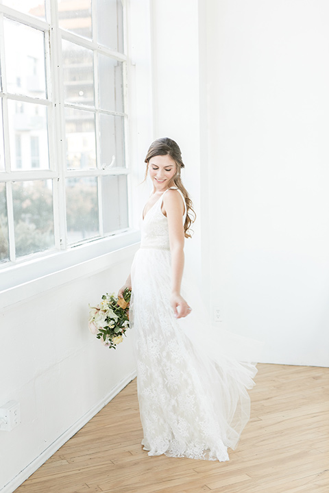 bride by the windows, wearing a flowing white gown with a lace detailing and straps