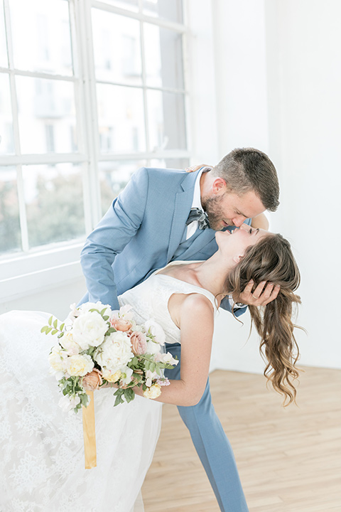 groom dipping the bride, the bride in a flowing white gown with a lace detailing and straps.  The groom in a light blue suit with a grey velvet bow tie