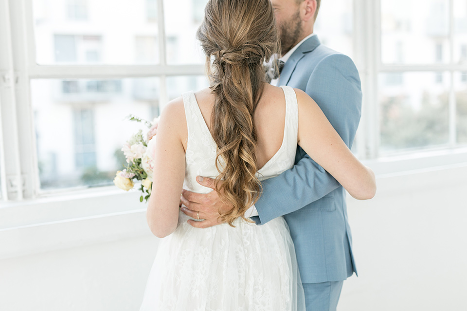  groom holding the bride and spinning her around, the bride in a flowing white gown with a lace detailing and straps.  The groom in a light blue suit with a grey velvet bow tie 