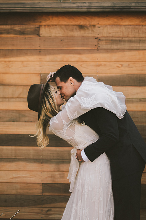 bride in a lace bohemian style gown with long flowing sleeves and a wide brimmed hat groom in a dark grey notch lapel suit with a black bow tie