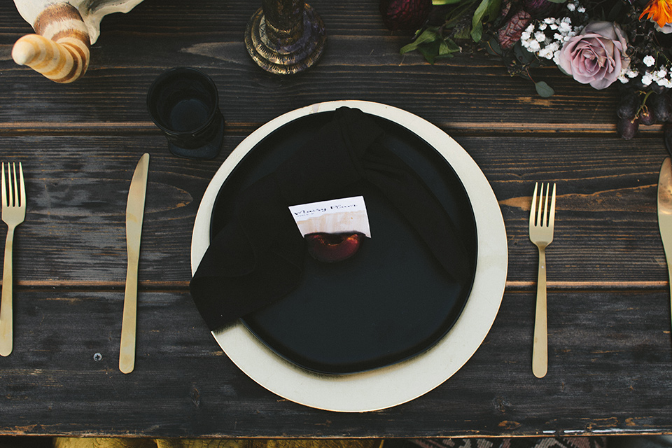  bohemian wooden table with big full flower décor with burgundy details and black and gold flatware and linens