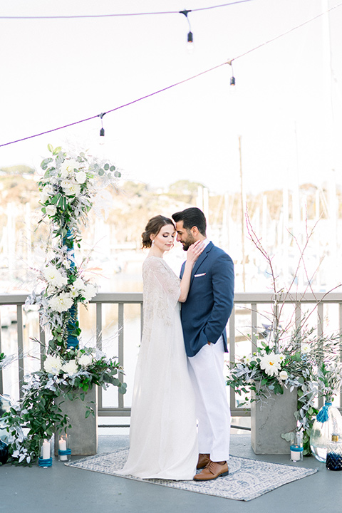  bride-in-a-flowing-gown-with-a-crystal-bodice-and-hair-in-a-loose-bun and the groom in a blue suit jacket with white pants and a floral long tie
