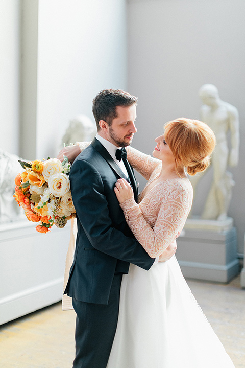  bride in a white ballgown with a crystal bodice and long sleeves with her hair in a low bun and the groom in a navy blue tuxedo with black shawl lapel design and black bow tie