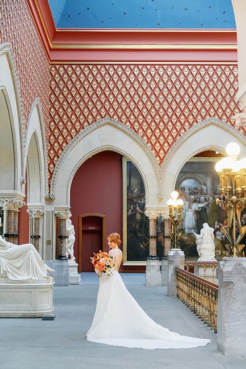  bride in a white ballgown with a crystal bodice and long sleeves with her hair in a low bun standing in the museum