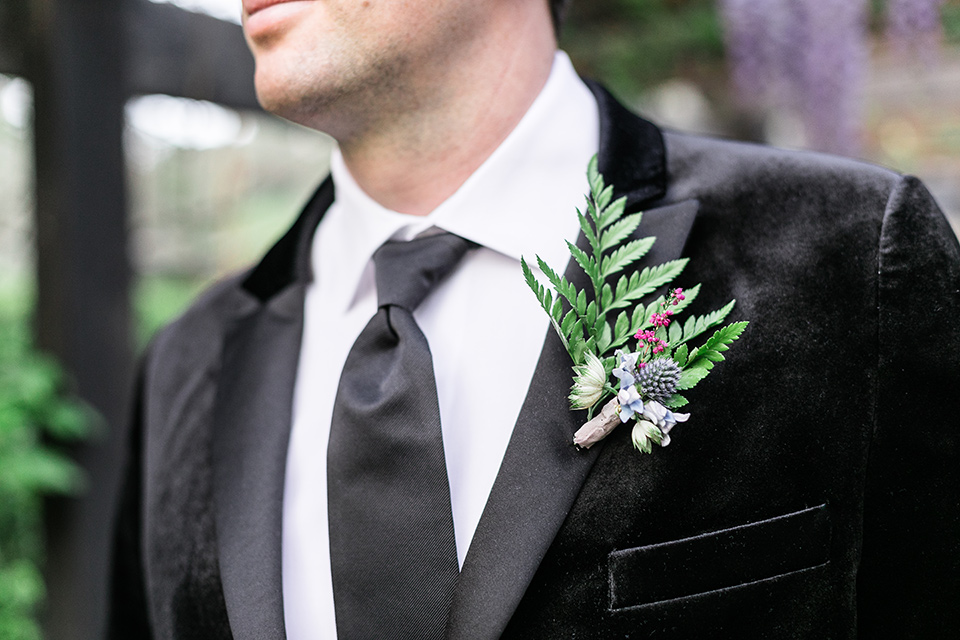  the groom in a black velvet tuxedo and a black long tie 