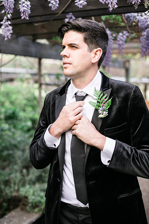  the groom in a black velvet tuxedo and a black long tie