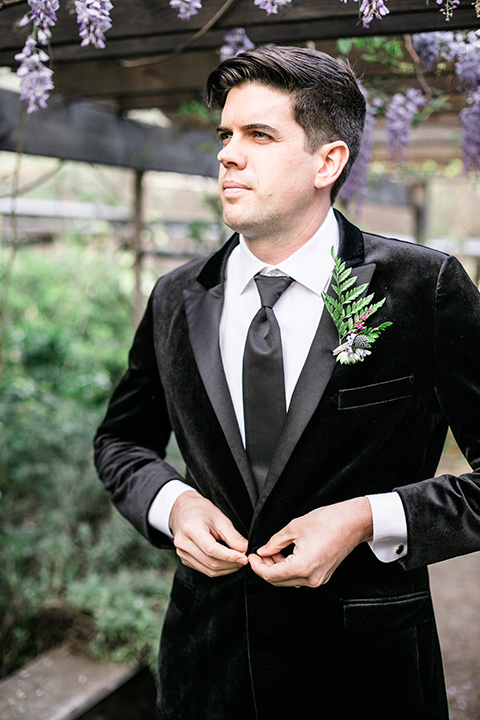  the groom in a black velvet tuxedo and a black long tie 