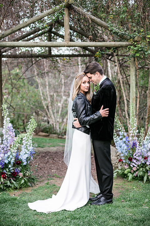 bride in a white lace gown and long sleeves and the groom in a black velvet tuxedo and a black long tie sitting together at the sweetheart table