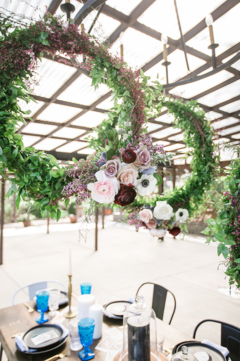  wooden table design with royal blue linens and circular floral hedges overhead 
