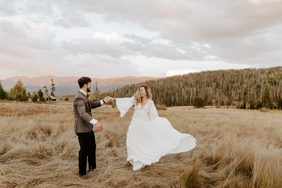  bride in a white lace gown with long flowing sleeves and a high neckline and the groom in a café brown suit coat with blue pants and a gold velvet bow tie