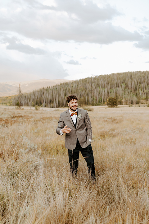  the groom in a café brown suit coat and blue pants with a gold velvet bow tie 