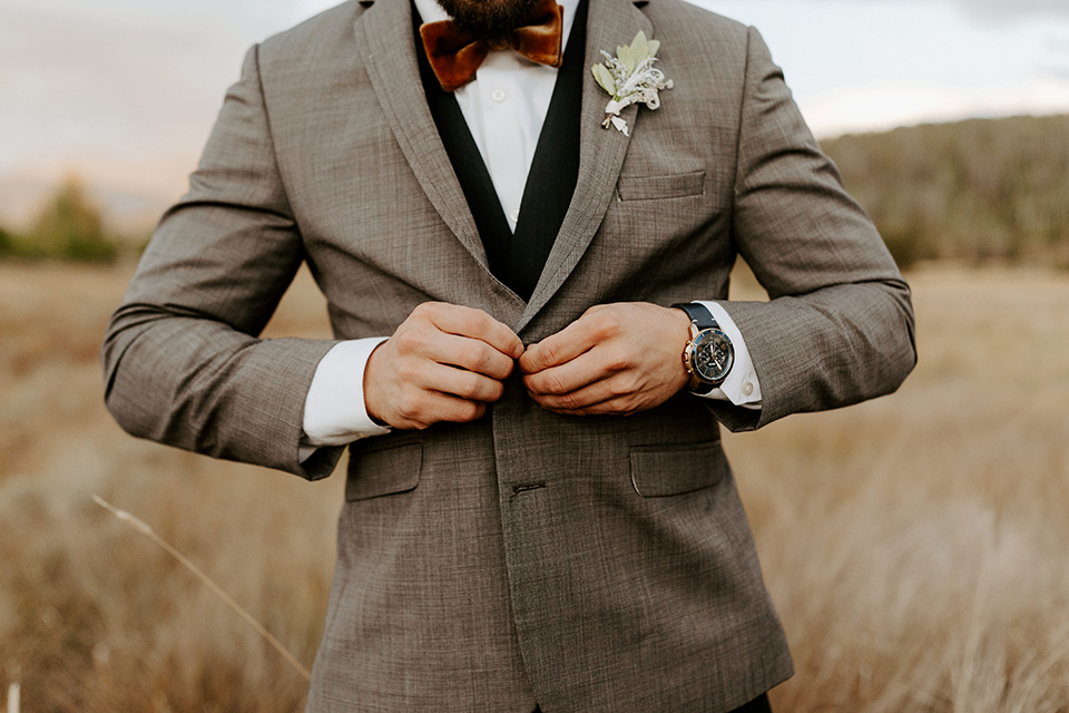  the groom in a café brown suit coat and blue pants with a gold velvet bow tie 