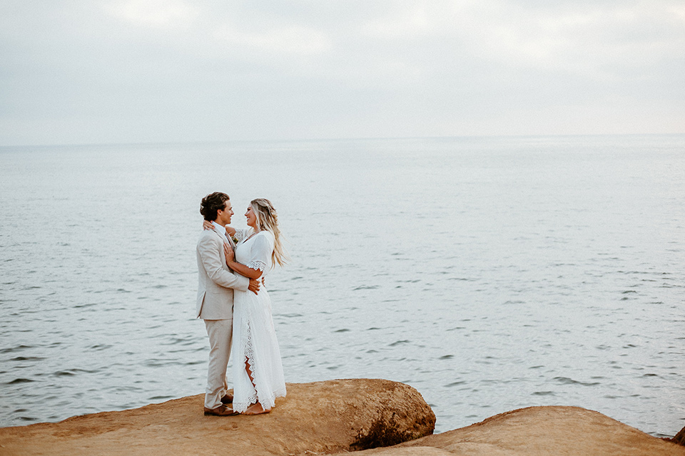  bride in a bohemian white lace gown and the groom in a light tan suit with a caramel long tie