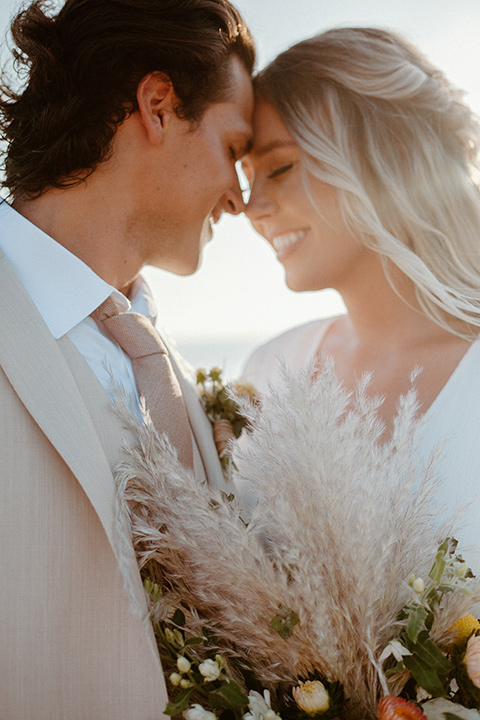  bride in a bohemian white lace gown and the groom in a light tan suit with a caramel long tie 