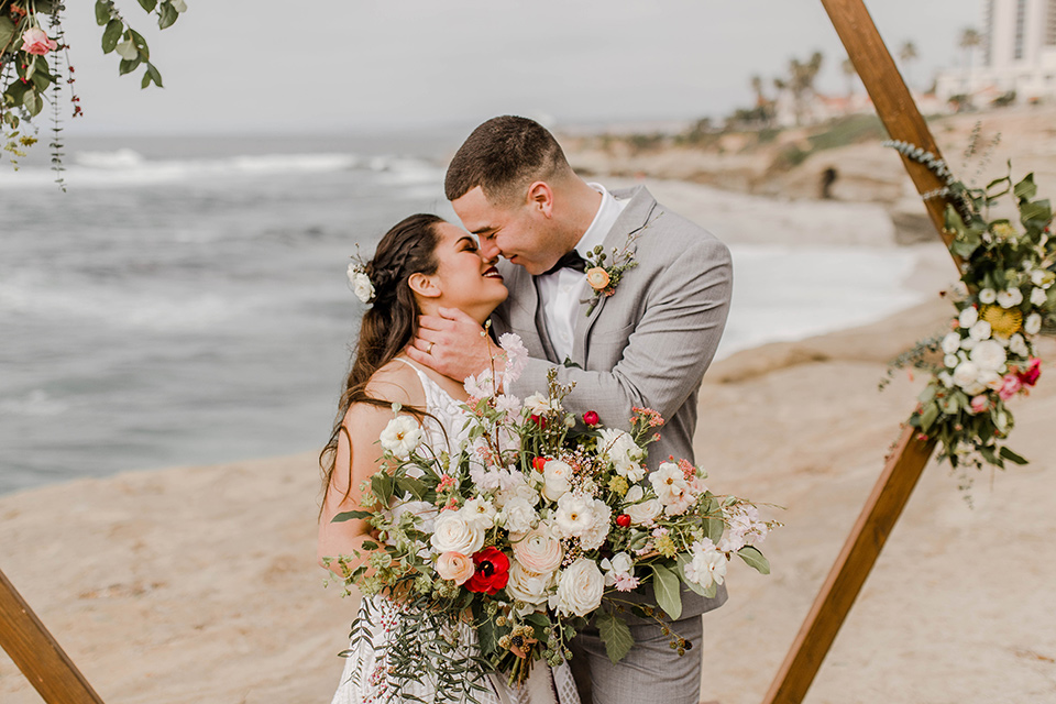  bride in a white gown with a flowing white skirt and low cut back and the groom in a light grey suit and charcoal bow tie at the ceremony