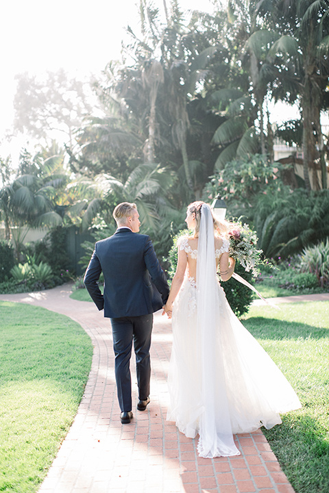  bridal gown with a lace and crystal design on it with long sleeves with the groom in a navy shawl lapel tuxedo with a black satin lapel walking away