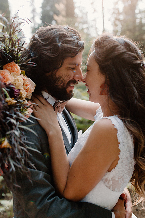  bride in a lace white gown with lace straps and a formfitting bodice and the groom in a café brown suit with a gold velvet bow tie