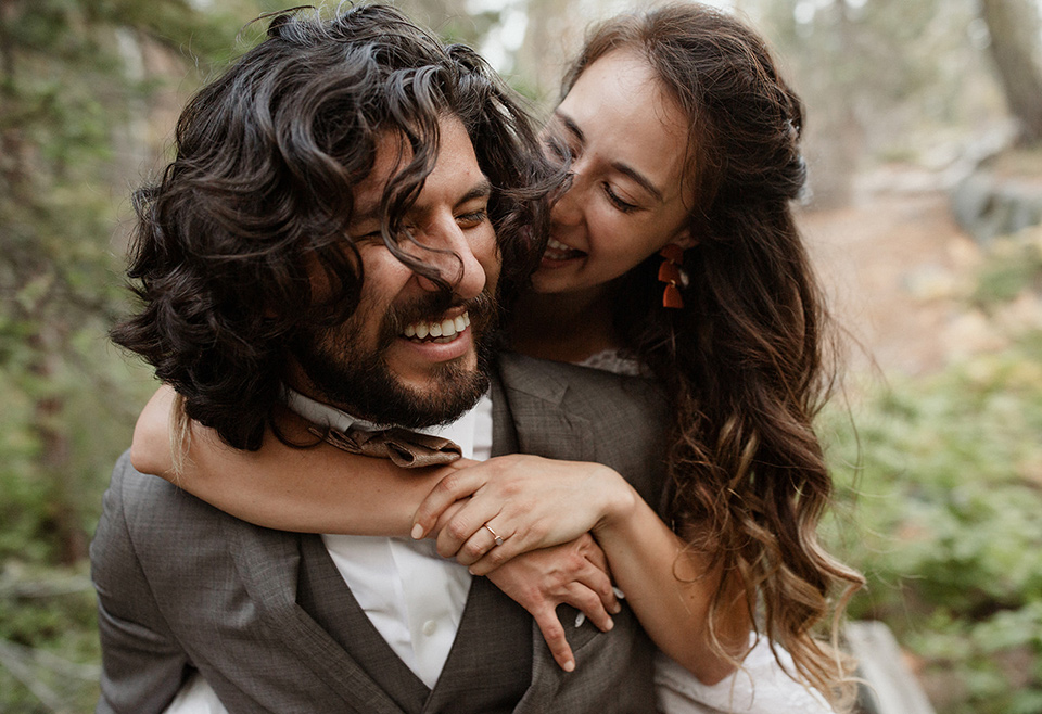  bride in a lace white gown with lace straps and a formfitting bodice and the groom in a café brown suit with a gold velvet bow tie 